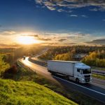 White trucks driving on the highway winding through forested landscape in autumn colors at sunset