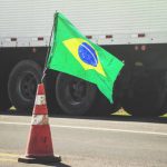 Brazilian flag on a red traffic cone of a highway with a blurred truck on background. Image concept to the stoppage and protest of the truck drivers on the highways of Brazil.